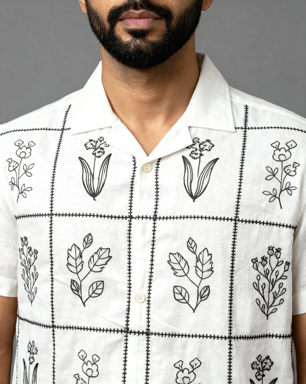 Men's white short-sleeve shirt with black floral embroidery, camp collar, and relaxed fit – front, close-up, and back view.